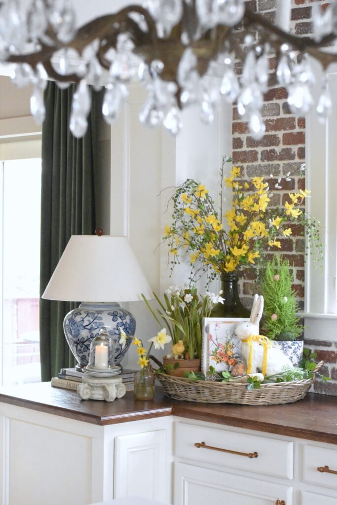 French Farmhouse basket tray styled for spring with forsythia branches, gardening books, paperwhites and farmhouse bunny with yellow velvet bow